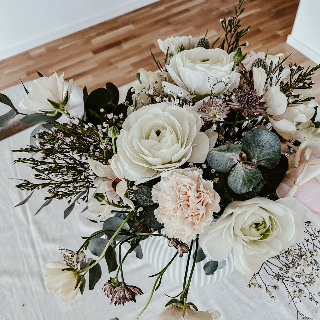 Bild på en blombukett i ljusa toner. I buketten finns blandannat nejlikor, ranunklar, fjärilsranunklar, vaxblommor, stjärnflocka och eukalyptus.